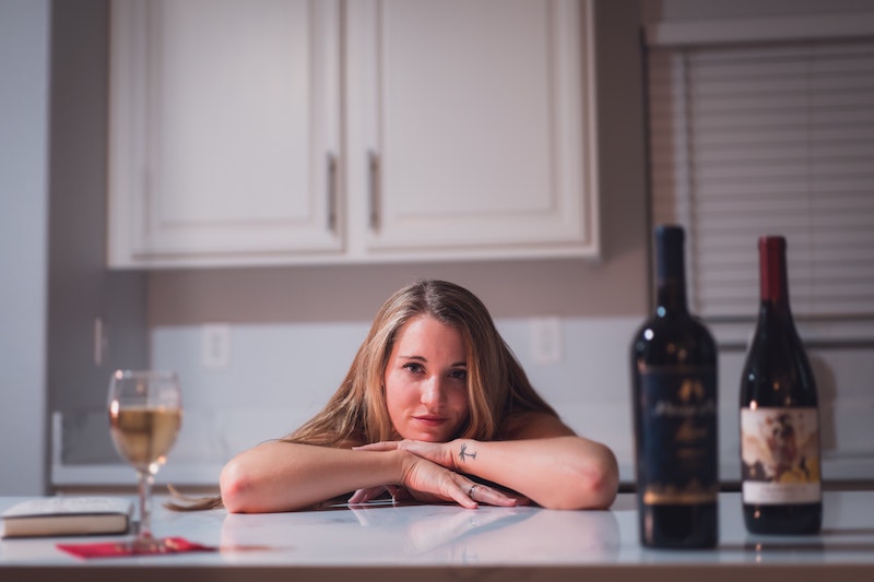 woman with her head down on the kitchen counter with alcohol bottles around her