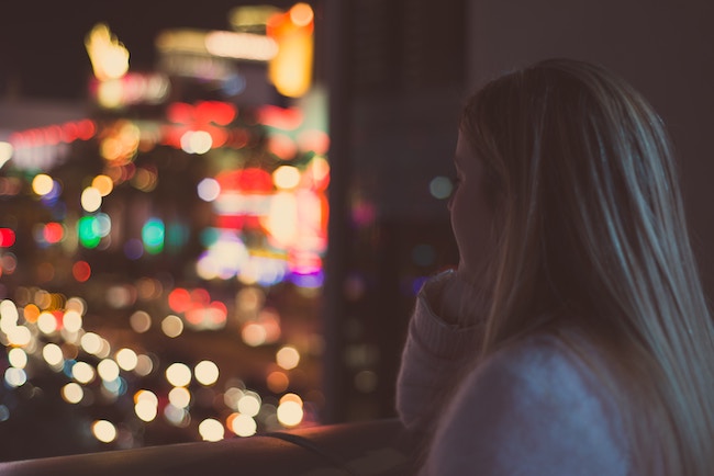 woman looking out the window with blurry lights in the window background
