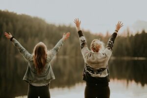 2 women with their hands up standing by a lake