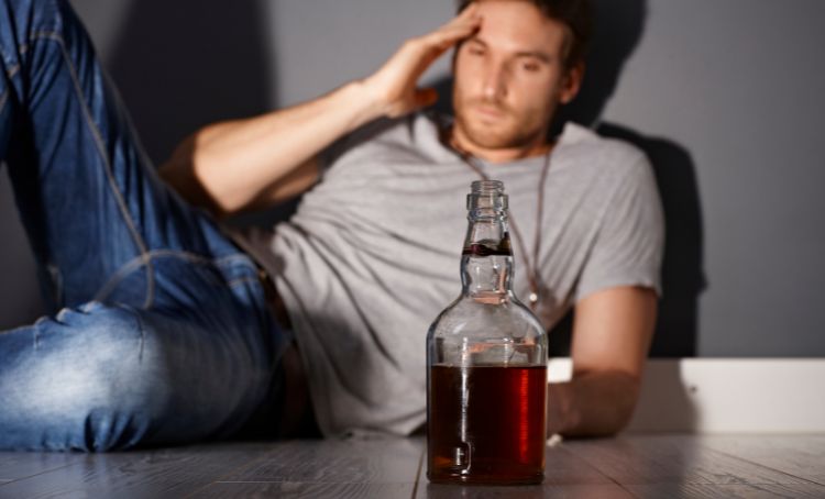 man staring at a bottle of alcohol and rubbing his temple - pregabalin and alcohol - Step by Step Recovery